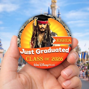 May include: A round button featuring a portrait of Captain Jack Sparrow wearing a graduation cap. The button has the text "Just Graduated CLASS OF 2026" and "JOSHUA". The background includes the Walt Disney World logo and a scenic view.