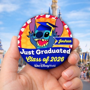 Op de afbeelding: Een ronde button met Stitch uit Lilo & Stitch met een afstudeerhoed. De button leest "Just Graduated Class of 2026" met de naam "Joshua" en het Walt Disney World logo. De achtergrond is een Disney-park.
