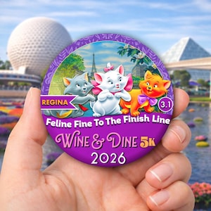 May include: A round purple button featuring three cartoon kittens, the Eiffel Tower, and text that reads: REGINA, Feline Fine To The Finish Line, WINE & DINE 5k, and 2026. The button also displays the number 3.1 in a small purple circle.