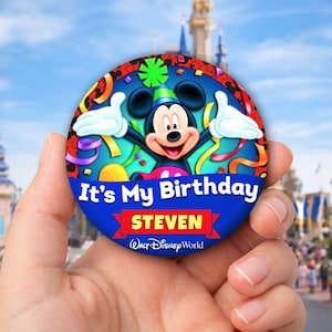 May include: A round, blue button featuring Mickey Mouse with the text "It's My Birthday" and the name "STEVEN". The button has a colorful confetti and streamer design, with the Walt Disney World logo at the bottom.