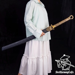 May include: A sword with a black textured scabbard and a gold-colored metal hilt featuring intricate dragon engravings and a circular pommel. The hilt guard displays a detailed relief design. A logo with the text SteelHarmonyCrafts is visible.
