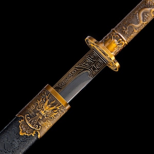 Pode incluir: Close-up de uma espada decorativa com punho e detalhes dourados. A lâmina é prateada e o punho apresenta um desenho de dragão. A bainha é preta com um padrão texturizado.