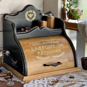 May include: A black and natural wood bread box with a roll-top door featuring the text BOULANGERIE LAFFONT JNE PATISSERIE in white lettering. The unit includes an upper shelf with a bee and laurel wreath emblem and a black metal handle.