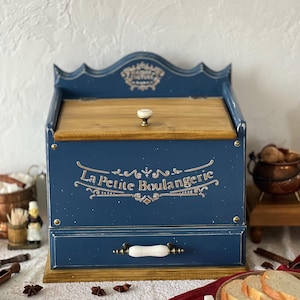 Könnte beinhalten: Eine marineblaue Brotdose aus Holz mit einer hellen Holzplatte und einem Sockel. Die Box hat eine Schublade und einen dekorativen Griff. Die Worte "La Petite Boulangerie" sind in goldener Schrift auf der Vorderseite geschrieben.