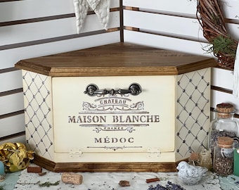 May include: A corner storage chest with a dark wood top and base, featuring cream-coloured panels with a black lattice pattern. The front panel displays the text CHATEAU MAISON BLANCHE FRANCE MÉDOC in black lettering and includes a dark metal handle.