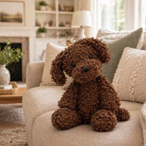 Peut inclure: Un jouet en peluche en forme de chien marron avec des oreilles tombantes et un nez noir est assis sur un canapé beige. Le jouet en peluche est fait d'un matériau bouclé texturé. Des coussins décoratifs et une couverture sont derrière le jouet.