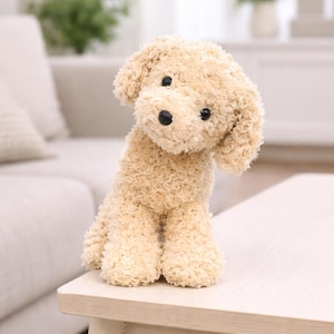 Peut inclure: Un chien en peluche avec une fourrure bouclée brun clair. Le chien a des yeux noirs et un nez noir. Il est assis sur une surface en bois de couleur claire. L'arrière-plan est flou, montrant un canapé et un coussin.
