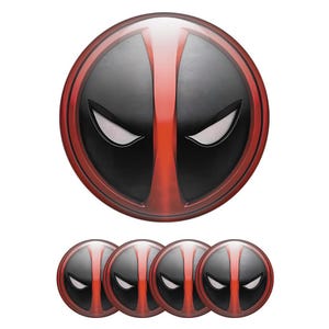 Puede incluir: Un conjunto de cinco calcomanías circulares con el diseño de la máscara de Deadpool. El diseño incluye un fondo negro, una franja roja vertical y ojos blancos. Las calcomanías están dispuestas con una grande y cuatro más pequeñas.