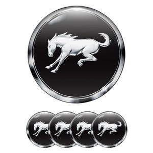 May include: A set of five black and silver emblems featuring a white running horse. The horse is in a dynamic pose, set against a black background within a silver circular frame. The emblems are likely for automotive or decorative use.