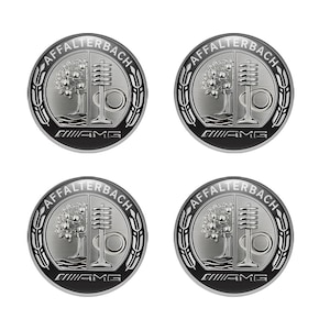 Op de afbeelding: Vier ronde emblemen met een zilver en zwart ontwerp. Elk embleem heeft bovenaan de tekst "AFFALTERBACH", in het midden een boom en een gestileerd ontwerp en onderaan de letters "AMG". De emblemen zijn omgeven door een zwarte rand.