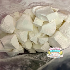 May include: A close-up of a clear bag filled with large, irregular chunks of white material. The chunks have a rough, textured surface. A colorful sticker with the text "Sassy Scents Crunch Cornstarch Chunks" is visible.