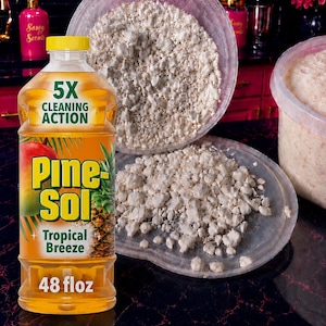 May include: A 48 fl oz bottle of Pine-Sol Tropical Breeze cleaning liquid with a yellow cap, featuring a pineapple and mango graphic, next to a clear plastic container filled with small, off-white, irregular, crumbly solid pieces.