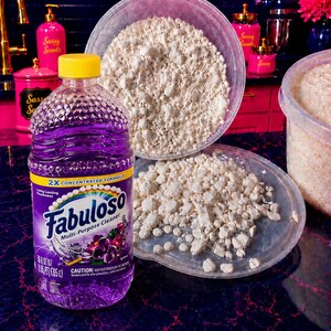 May include: A clear plastic bottle of purple Fabuloso multi-purpose cleaner with a yellow cap, positioned next to a clear plastic bowl and lid filled with small, irregular, off-white solid chunks. The label reads 2X Concentrated Formula.