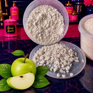 May include: A clear plastic container filled with white, granular wax melts, with a second lid resting below it. A bright green apple and a single apple slice with green leaves are positioned next to the container on a dark, mottled surface.