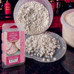 May include: A clear plastic clamshell package of Frosted Sugar Cookie soy blend wax melts with a pink label, next to a large clear plastic container filled with small, irregular, off-white wax chunks and a matching lid covered in more wax pieces.