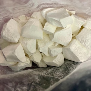 Puede incluir: Primer plano de una bolsa de plástico transparente llena de numerosos trozos blancos grandes de forma irregular. Los trozos tienen una superficie rugosa y texturizada y varían en tamaño. La bolsa es parcialmente visible, con un aspecto ligeramente translúcido.