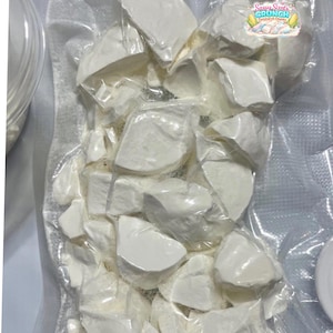 Op de afbeelding: Een vacuüm verpakte plastic zak met talloze onregelmatige, massieve witte maïszetmeelstukken. Een klein rond logo in de rechterbovenhoek bevat de tekst Sassy Scents Crunch Cornstarch Chunks met een illustratie van maïskolven.