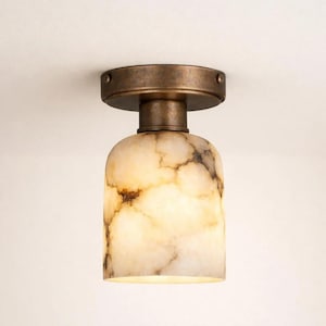 Op de afbeelding: Een plafondlamp met een bronzen metalen basis en een cilindrische kap. De kap is gemaakt van een crèmewit materiaal met bruine adering, waardoor een marmer effect ontstaat. De lamp is ontworpen voor gebruik binnenshuis.