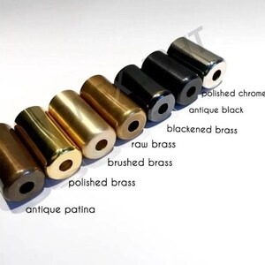 Puede incluir: Una variedad de objetos cil&iacute;ndricos de metal en varios acabados, incluyendo cromo pulido y negro antiguo. La imagen muestra una gama de colores desde marr&oacute;n oscuro hasta plateado, con etiquetas que indican cada acabado. Probablemente se trata de herrajes decorativos.