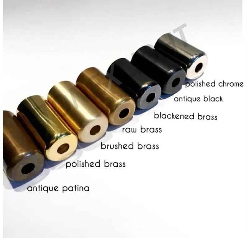 Puede incluir: Una variedad de objetos cil&iacute;ndricos de metal en varios acabados, incluyendo cromo pulido y negro antiguo. La imagen muestra una gama de colores desde marr&oacute;n oscuro hasta plateado, con etiquetas que indican cada acabado. Probablemente se trata de herrajes decorativos.