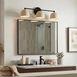 Puede incluir: Un tocador de ba&ntilde;o moderno con un espejo rectangular grande y una l&aacute;mpara de tres luces. La l&aacute;mpara tiene un marco negro y pantallas beige en forma de c&uacute;pula. El tocador cuenta con una encimera de m&aacute;rmol, un mueble de madera y accesorios negros.