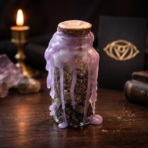 May include: A clear glass jar filled with dried herbs and sealed with a cork stopper. The jar is adorned with dripping lavender wax. A lit candle and a book with a golden eye symbol are in the background.