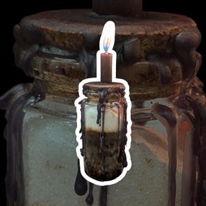 May include: A small glass jar with a cork stopper, filled with layers of sand and other materials. A lit black candle is attached to the cork. The jar is covered in black wax drippings, creating a gothic or mystical aesthetic.