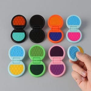 Puede incluir: Una colección de ocho aplicadores de tiza para el cabello compactos y coloridos. Cada aplicador es de un color diferente, incluyendo naranja, negro, azul, rosa, verde, morado y amarillo. Los aplicadores están abiertos, revelando la tiza en su interior. Uno es sostenido por una mano.