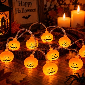 Peut inclure: Une guirlande lumineuse composée de dix citrouilles LED orange, chacune arborant un visage de jack-o'-lantern sculpté. Ces petites citrouilles en plastique brillant sont reliées par un fil fin et transparent pour une décoration d'Halloween.