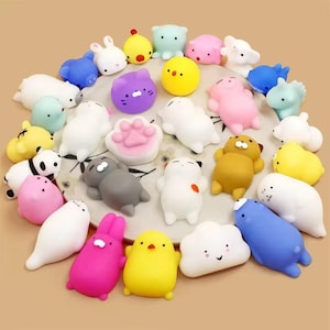 May include: A selection of colourful, squishy animal toys in various shapes, including bunnies, cats, and bears. The toys are in shades of pink, yellow, blue, and white, arranged on a patterned surface. These are ideal for children.