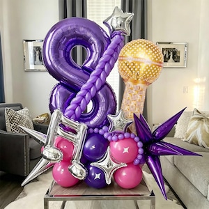 May include: A balloon arrangement featuring a large purple number eight balloon, a gold microphone balloon, and a silver musical note balloon. The display includes smaller purple and pink balloons, silver star accents, and purple starburst balloons.