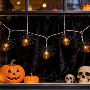 May include: A string of decorative spider-shaped lights featuring black plastic spider bodies with glowing amber bulbs. The lights are connected by a thin white wire, creating a series of illuminated arachnids for seasonal display.
