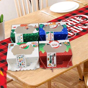 May include: Four square cardboard gift boxes with clear windows, featuring festive holiday designs including a reindeer, snowman, elf, and Santa Claus. Each box has a hanging tag with the text Merry Christmas printed on the front.