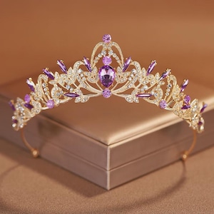 Peut inclure: Un diadème doré présentant un design complexe en filigrane métallique orné de nombreuses pierres transparentes et de gemmes violettes. La pièce centrale est une pierre violette en forme de poire, entourée d'accents violets ronds et marquise.