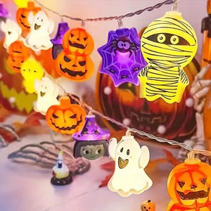 May include: A string of Halloween-themed LED lights featuring various plastic shapes including orange pumpkins, white ghosts, a purple spider web with a black spider, a yellow mummy, and a purple witch hat, all connected by a thin clear wire.