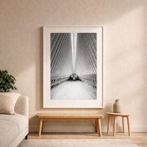 May include: Black and white photograph of a modern architectural interior. The image features a long, symmetrical corridor with a high, ribbed ceiling. The photograph is framed and displayed on a wall, with a bench and side table in front.