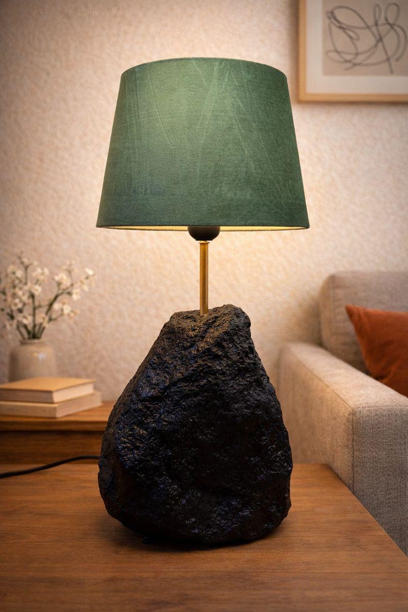 May include: A modern table lamp with a dark green lampshade and a black, textured base. The lamp has a gold-colored stem and sits on a wooden table. The lamp is a decorative home decor item.