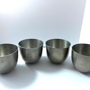 May include: Four small, brushed metal bowls with a rounded shape. The bowls are silver in color and have a smooth, matte finish. The bowls are arranged in a row, with the opening of each bowl facing up.
