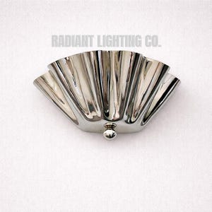 Könnte beinhalten: Eine polierte silberne Wandleuchte mit einem wellenförmigen Design. Die Leuchte hat einen abgerundeten Sockel mit einem kleinen, kugelförmigen Detail. Der Text "RADIANT LIGHTING CO." ist darüber gedruckt.