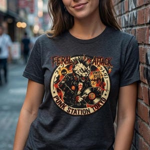 Puede incluir: Camiseta gris oscuro con un gráfico de un gato con chaqueta de cuero sosteniendo un disco de vinilo. El diseño incluye las palabras "FERAL ATTACK", "PUNK STATION TOKYO" y "VINYL RIOT" en un emblema circular.