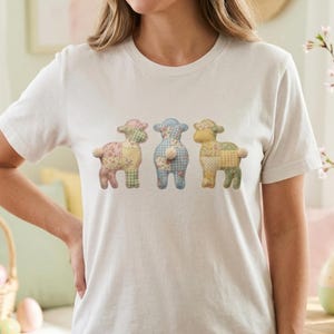 Puede incluir: Camiseta blanca con tres diseños de ovejas de patchwork en colores pastel. Las ovejas tienen estampados florales, de cuadros y de lunares. Esta camiseta informal es adecuada para el uso diario, ideal para Pascua o primavera.