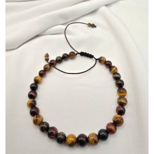 May include: A beaded bracelet featuring a variety of earth-toned beads, including shades of yellow, brown, and burgundy. The bracelet is strung on a black cord with an adjustable sliding knot closure. The beads are round and polished.