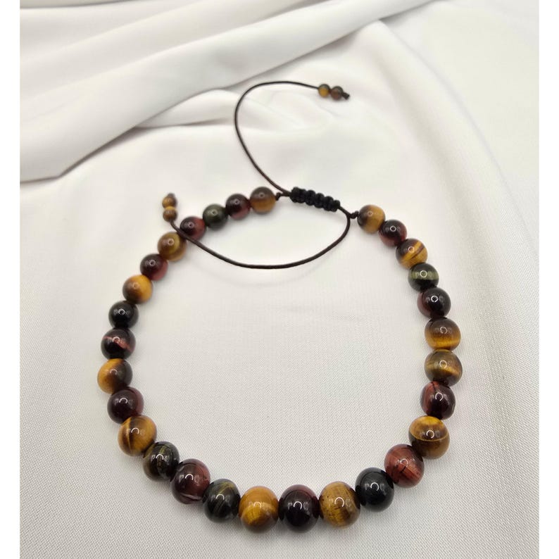 May include: A beaded bracelet featuring a variety of earth-toned beads, including shades of yellow, brown, and burgundy. The bracelet is strung on a black cord with an adjustable sliding knot closure. The beads are round and polished.