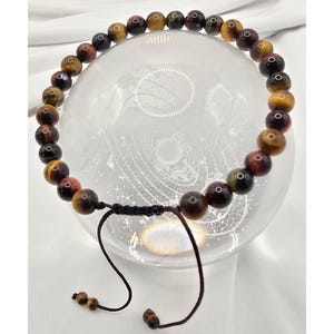 May include: A beaded bracelet featuring tiger's eye gemstones in shades of brown, gold, and red. The bracelet is strung on a black cord with an adjustable sliding knot closure. The gemstones are round and polished, with a natural, earthy appearance.