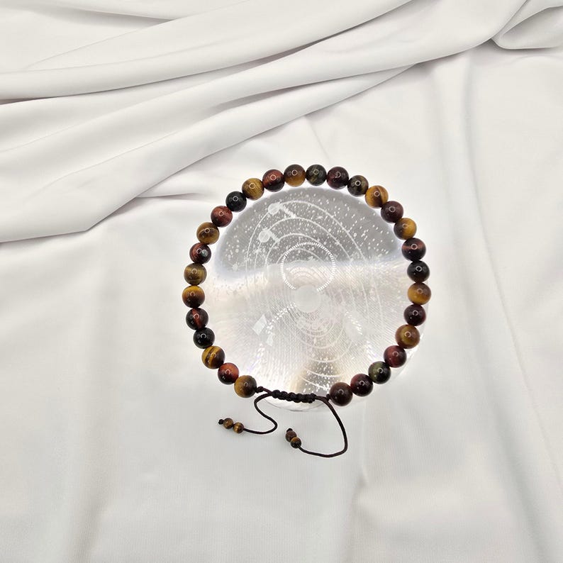 May include: A beaded bracelet featuring tiger's eye stones in shades of brown, red, and gold. The bracelet is strung on a black cord with an adjustable sliding knot closure. The beads are approximately 0.8 cm in diameter.