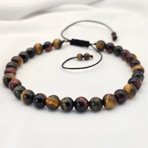 May include: A beaded bracelet featuring tiger's eye stones in shades of brown, gold, and red. The adjustable bracelet has a black cord closure. The beads are round and polished, creating a natural and earthy aesthetic.