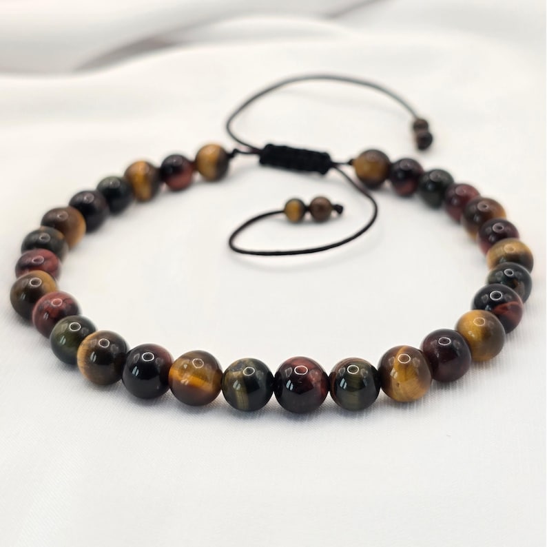 May include: A beaded bracelet featuring tiger's eye stones in shades of brown, gold, and red. The adjustable bracelet has a black cord closure. The beads are round and polished, creating a natural and earthy aesthetic.