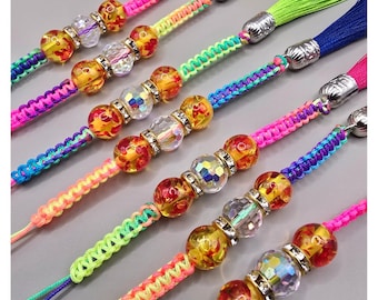 May include: Close-up of colorful beaded tassels. Each tassel features a vibrant color scheme, including pink, yellow, green, and blue. The tassels are adorned with decorative beads and silver-toned metal accents. The background is a solid gray.