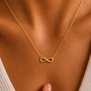 May include: A gold-toned necklace featuring a delicate chain and a central infinity symbol pendant. The metal has a smooth, polished finish. The word KRAFTIYA is printed in white capital letters at the bottom centre of the image frame.
