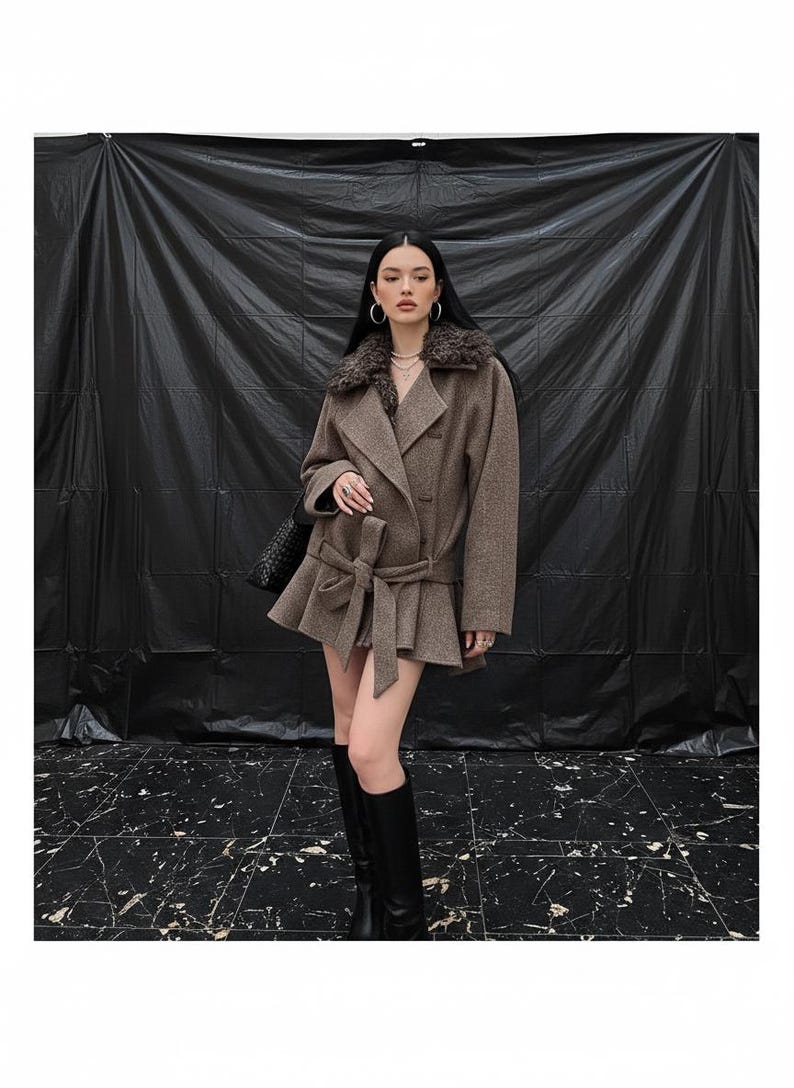 May include: A brown coat with a faux fur collar and a belted waist. The coat has a flared hem and is paired with black knee-high boots. The background is a black backdrop.